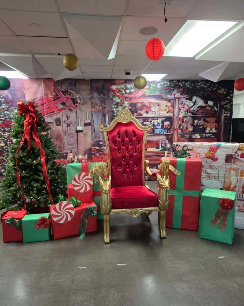 Red and gold Santa chair with gift boxes beside a Christmas tree.