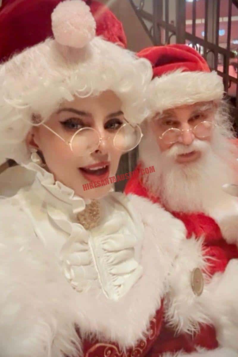 Santa and Mrs. Claus in Austin pose together in red-and-white costumes with round glasses.