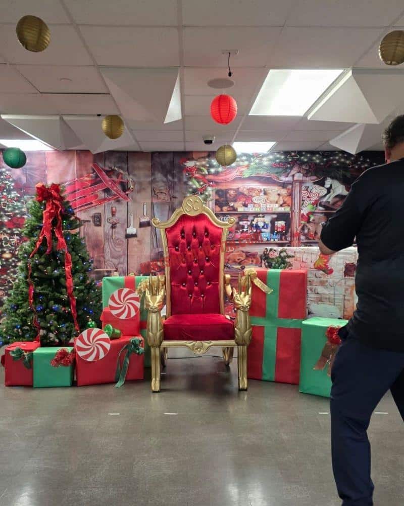 Santa photos set with a gold-and-red chair, wrapped gifts, Christmas tree, and paper lanterns indoors.