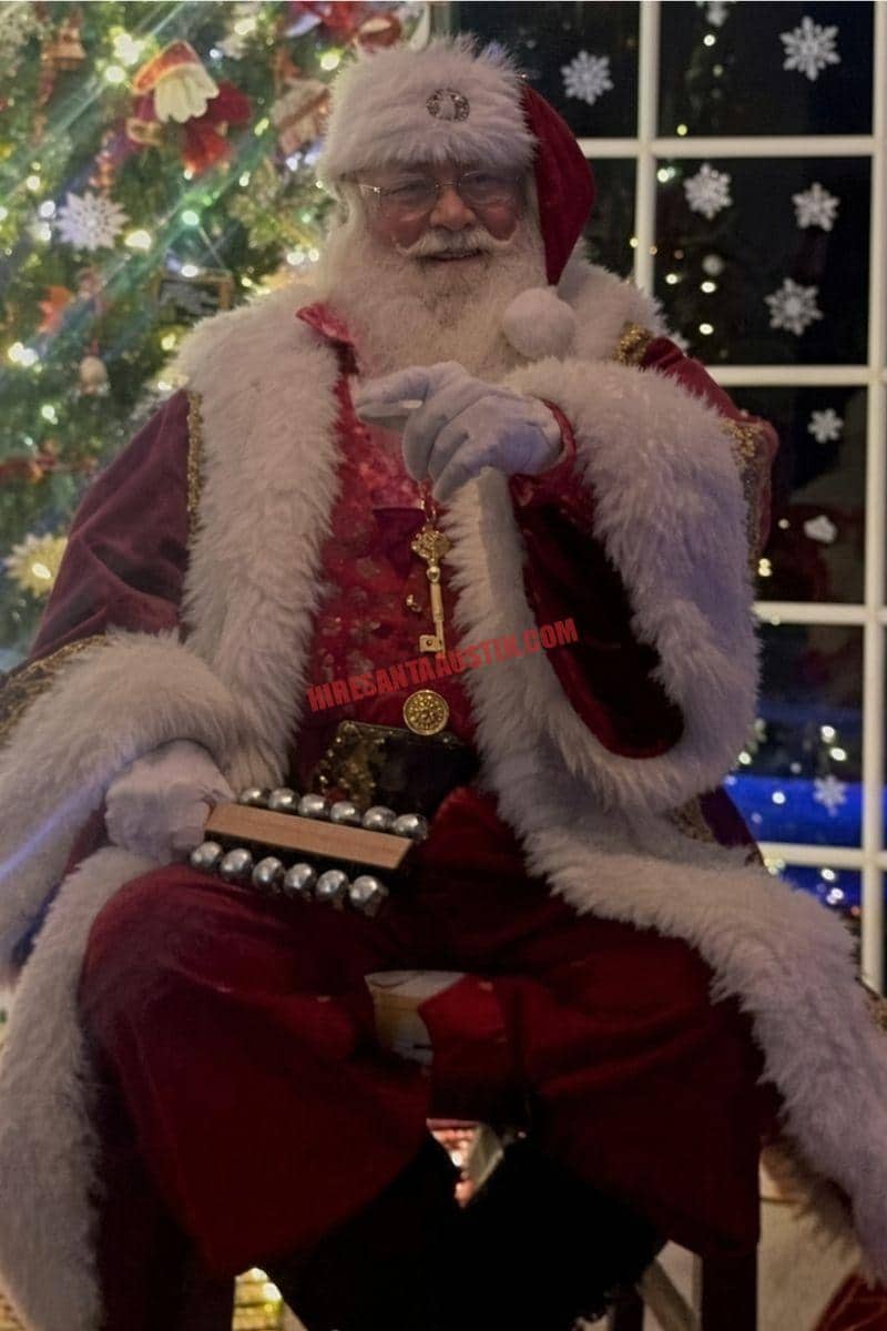 Hire Santa Cedar Park: Santa in a burgundy coat holds sleigh bells by a tree and a snowflake window.